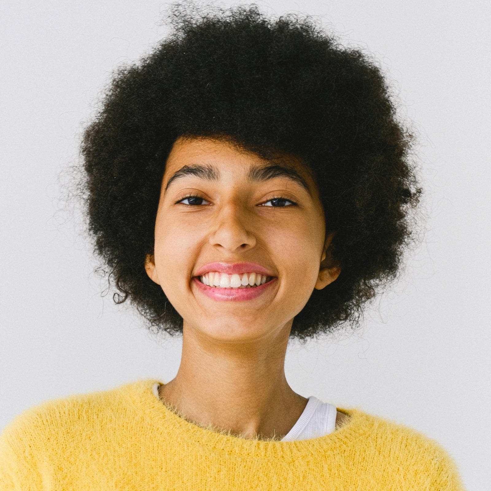 Young person with curly hair smiling brightly in yellow sweater