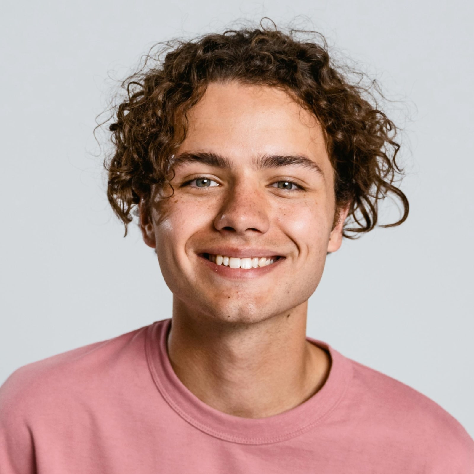 Smiling person with curly hair wearing pink shirt against white background