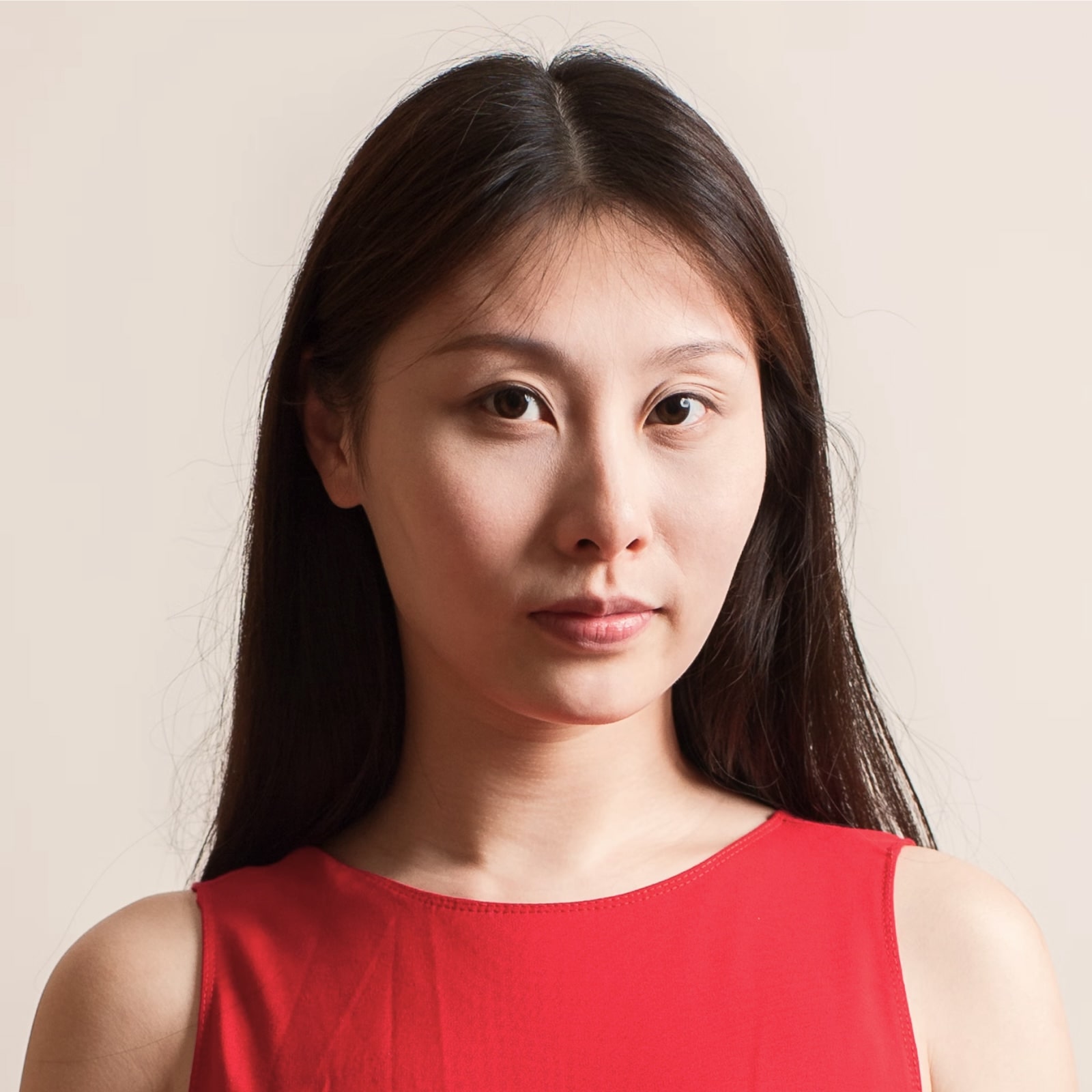 Woman in bright red top against neutral background looking directly forward